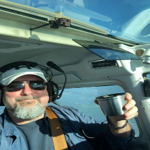 Jim Coffey II wearing a pilot headset and raising a coffee cup inside an aircraft
